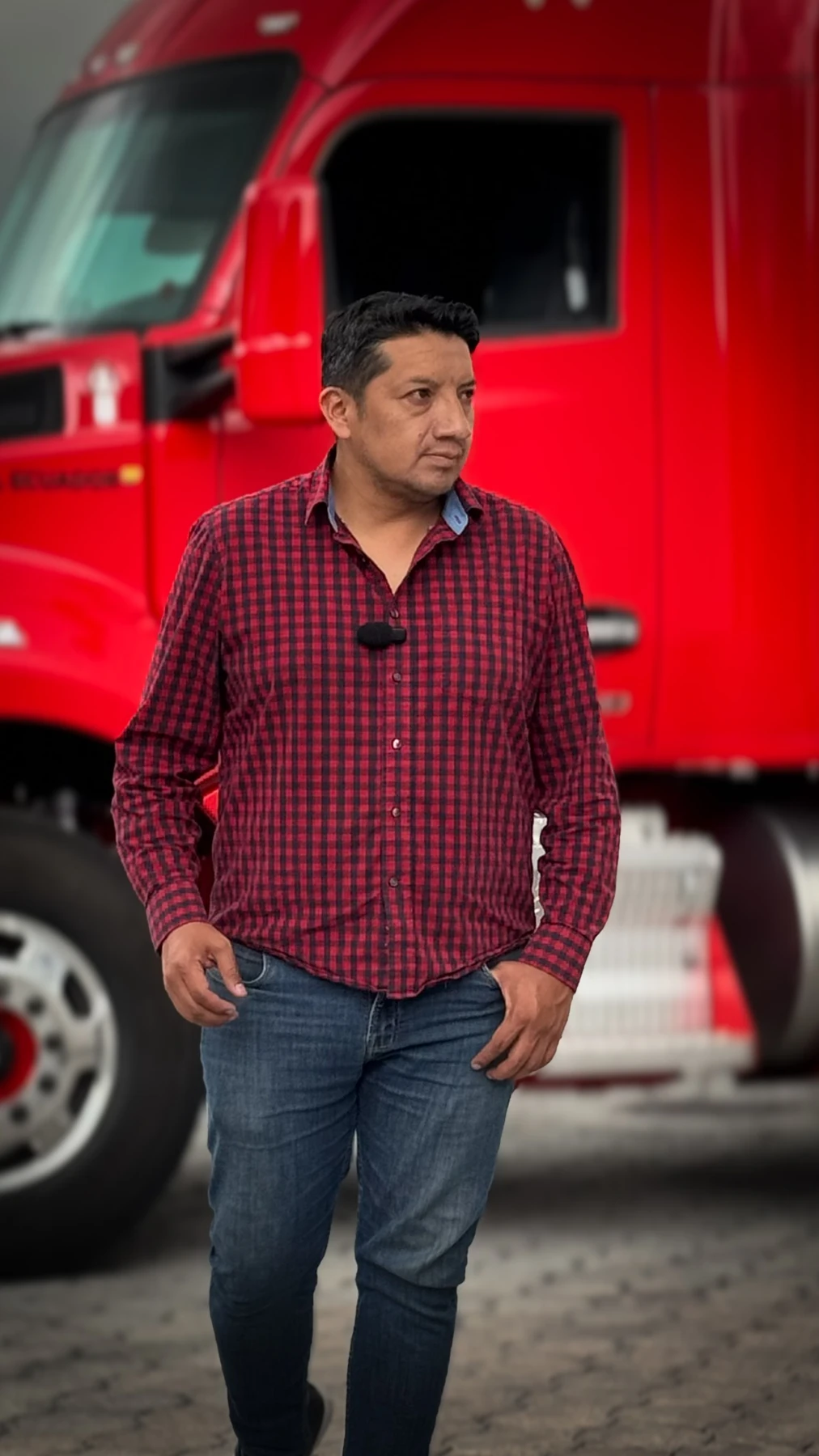 Migue Santamaría de pie, con camisa roja, frente a un camión rojo